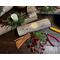 A Christmas yule log candle centerpiece. It is made from upcycled wood with a white candle, greenery, and berries arranged on the top.  